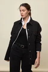 Sobrecamisa de denim negro con calce amplio, cuello clásico, bolsillos frontales con solapa y cierre de broches metálicos.