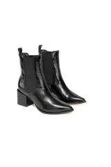 Botas de caña baja tipo chelsea de cuero charol negro con acabado brillante, punta fina y taco cuadrado. Cuentan con paneles elásticos laterales y presilla trasera.