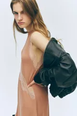 Vestido midi sin mangas de punto suave, con escote redondo y bajo asimétrico. Presenta detalles de encaje en las sisas, en la parte frontal y en el ruedo.
