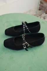 Ballerina de gamuza negra con puntera cuadrada y doble tira cruzada en el empeine con ojales metálicos y hebillas ajustables.