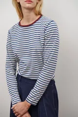 Remera de manga larga con diseño de rayas horizontales en azul y blanco, destacada por un cuello redondo en color bordó con costuras a la vista.