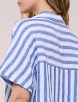 Camisa de algodón con rayas verticales en tonos verde, rosado y blanco. Tiene mangas cortas amplias, escote en V con solapa y botones frontales, y detalle de nudo en el bajo.