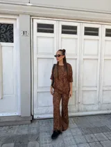 Conjunto de dos piezas compuesto por una remera de manga corta y un pantalón de corte acampanado, ambos confeccionados en lanilla con estampado animal print en tonos marrones.