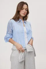 Camisa de manga larga con diseño de rayas verticales en tonos celestes, blancos y marrones, confeccionada en tejido semitransparente con cuello camisero y cierre frontal de botones.