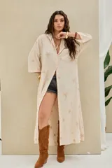 Camisola larga de lino beige con bordados de palmeras y caracoles dorados, corte oversize, mangas tres cuartos y bolsillos en el frente.