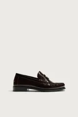 Mocasín de vestir color marrón oscuro, fabricado en cuero, con detalle de antifaz en el empeine y suela a tono con ligero tacón.