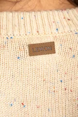Cardigan color crema con diseño moteado en azul y naranja, de tejido de punto con textura. Tiene cuello redondo, cierre frontal con broches y bolsillos de parche.