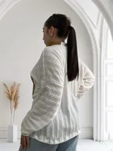 Polera blanca de tejido trenzado con cuello alto de cuero marrón y bolsillo de cuero marrón con textura de cocodrilo.