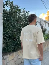 Remera negra de corte oversize con estampa gráfica en la espalda. El diseño presenta una silueta lineal de un ángel, el logo Dropz Corp. en tipografía script, un bloque de microtexto y un código de barras gráfico.