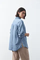 Camisa de jean en tencel con silueta amplia, hombros caídos, cuello clásico y cierre frontal con botones. Presenta ruedo curvo con tajos laterales y pliegue en la espalda.