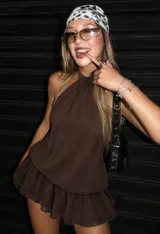 Vestido corto color chocolate con cuello halter, hombros descubiertos, silueta blusón y falda mini con volados, incluye short interno.