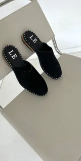 Mules de cuero negro con tachas plateadas en el borde de la suela y plantilla con logo estampado.