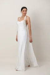 Vestido largo de seda natural color blanco, con escote halter tipo Marilyn y espalda descubierta. Presenta un elaborado bordado a mano con pedrería en la parte superior y caída fluida.