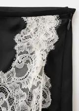 Falda corta de satén negro con detalle de delicada puntilla blanca en el borde inferior.