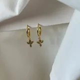 Par de aros dorados con forma de argolla y dije colgante con forma de flor de cuatro pétalos con incrustaciones de strass.
