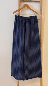 Pantalón de corte ancho y relajado, confeccionado en lino con diseño de rayas verticales. Presenta cintura elástica con cordón de ajuste y bolsillos laterales.