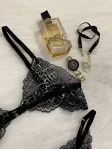 Conjunto de lencería compuesto por bralette triangular y tanga, confeccionado en encaje bitono negro y blanco. El bralette presenta cierre frontal con broche de gancho y breteles regulables. La tanga es de estilo colaless con laterales regulables mediante herrajes metálicos.