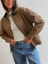 Campera de gabardina color beige con cierre frontal y cuello en contraste color negro. Presenta un diseño minimalista con bolsillos delanteros funcionales y calce cómodo.