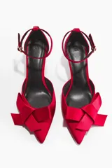 Zapatos de tacón de satén color rojo, con puntera fina adornada con una moña grande y tira ajustable al tobillo.