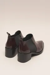 Botín chelsea de cuero vacuno color bordó con acabado charol, punta fina y elástico lateral negro. Posee un taco ancho y bajo de goma.