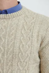 Sweater de tejido de punto color beige claro, con diseño de trenzas (aranes) en el frente y mangas de punto liso. Tiene cuello redondo.