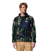 Campera polar de textura tipo corderito con estampado camuflado en tonos verde, azul marino y beige. Presenta cierre frontal completo, cuello alto y un bolsillo frontal en el pecho con cierre y parche de la marca.