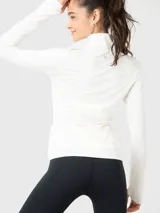 Buzo deportivo color crema de tela suave y delgada, con medio cierre frontal, cuello alto y mangas largas con orificios para los pulgares.