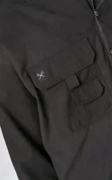 Camisa de manga larga color negro, estilo técnica con calce oversize. Presenta múltiples bolsillos frontales con solapa y detalle de tiras, un pequeño bordado de tijeras en el pecho izquierdo y botones en la cartera frontal y puños.