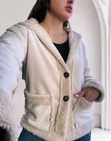 Campera de pana color crema con interior de piel sintética color beige. Tiene capucha, cierre con botones a presión, bolsillos laterales y puños con ribete de piel sintética.