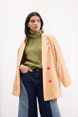 Blazer oversize confeccionado en lino, con diseño estampado combinado de rayas y cuadros en tonos naranja y blanco. Presenta solapas clásicas, hombros marcados y cierre frontal con cuatro botones a contratono.