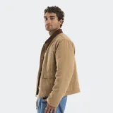 Campera estilo carpenter color beige con cuello de pana en contraste color marrón. Presenta cierre frontal con botones metálicos, bolsillos frontales con solapa y parche bordado con logo en el pecho. El interior cuenta con forro acolchado.