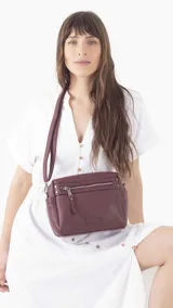 Bandolera color beige de símil cuero, con cierre principal, bolsillos interiores, bolsillo frontal y posterior con cierres, y bolsillos laterales. Incluye correa extensible.