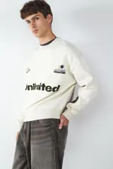 Buzo de cuello redondo con calce relajado, confeccionado en fleece. Presenta un diseño en color blanco con paneles laterales en contraste color gris oscuro, y estampados gráficos frontales con la palabra Unlimited.