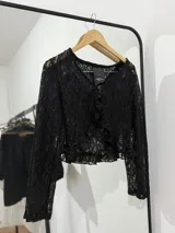 Blusa corta de encaje negro con mangas largas y volados en el frente.