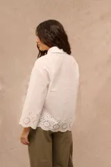 Camisa blanca de manga larga con diseño oversize, cuello camisero y cierre frontal de botones. Presenta detalles de bordado inglés calado en el ruedo y en los puños acampanados.