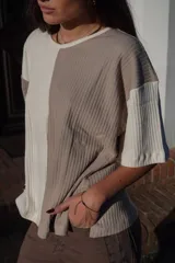 Remera de tejido de punto, manga corta, con diseño bicolor en negro y beige. La prenda es de corte holgado y presenta un ligero acanalado vertical.