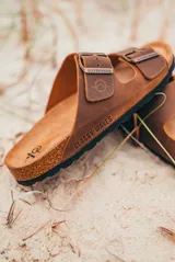 Sandalias marrones de cuero con plantilla de corcho, suela negra y doble tira con hebilla metálica ajustable.