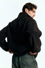 Buzo deportivo de polar negro, con cuello alto y cierre parcial frontal. Presenta mangas largas con puños ajustados y corte relajado.