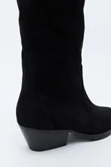 Bota texana de caña alta confeccionada en gamuza negra, con diseño de estilo western, costuras decorativas, tirador superior y taco bajo levemente inclinado.