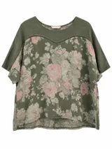 Blusa verde militar de manga corta con estampado floral en tonos rosados y beiges. Presenta cuello redondo y detalle de costura decorativa con calados en la parte superior del frente y las mangas.