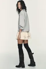 Vestido corto que combina una parte superior tipo sudadera gris de manga larga con puños, y una falda corta de volantes color crema. La parte superior es de tejido de punto jaspeado y la falda tiene dos capas de volantes.