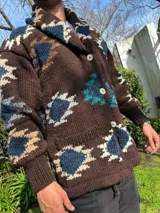 Saco de lana marrón con cuello esmoquin, cierre con botones y bolsillos delanteros. Diseño con motivos geométricos en tonos azul, beige y blanco.