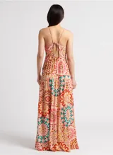 Vestido largo con estampado caleidoscópico en tonos rosa, rojo y verde. Presenta tirantes finos, escote en V, corte imperio y falda con volantes. Incluye detalle de trenzas en el pecho y la cintura que se anudan en la espalda descubierta.