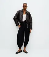 Pantalón de sastrería modelo aladim, color negro, confeccionado en crepé. Presenta pliegues en la cintura, corte holgado con piernas anchas que se estrechan en los tobillos y detalle de cinturón de cadena metálica.