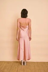 Vestido largo de satén color rosado, con escote halter drapeado, sin mangas y silueta fluida con tajo lateral.