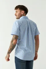 Camisa de manga corta con estampado de cuadros vichy en azul y blanco. Presenta cuello con botones, cierre frontal con botones y logo bordado en el pecho.