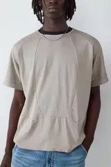 Camiseta de manga corta con corte amplio y diseño de costuras decorativas tipo piping en el frente. Presenta cuello redondo en color negro en contraste con el cuerpo de la prenda en tono beige.