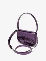Bolso compacto tipo bandolera para mujer, con asa corta para llevar al hombro y correa desmontable opcional para usar cruzado. Confeccionado en cuero con acabado espejado brillante color morado. Presenta placa oval D galvanizada en la solapa.