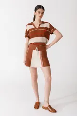 Falda corta de tejido de punto, color rojo coral, con un panel frontal en color rosado claro. Presenta un cordón de ajuste en la cintura y detalles de franjas verticales en verde azulado y rosado claro en el panel frontal.