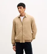 Campera tipo bomber de sarga color beige, con cuello inglés, cierre frontal de cremallera y puños y cintura ajustados con elástico en tono contrastante.